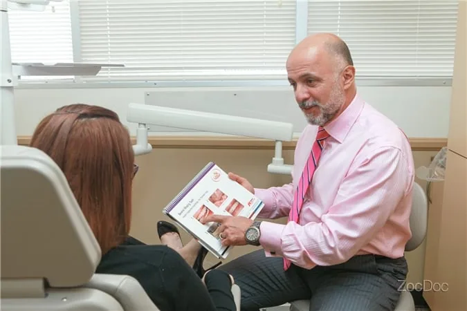 A dentist showing a brochure to a patient seated in a treatment room