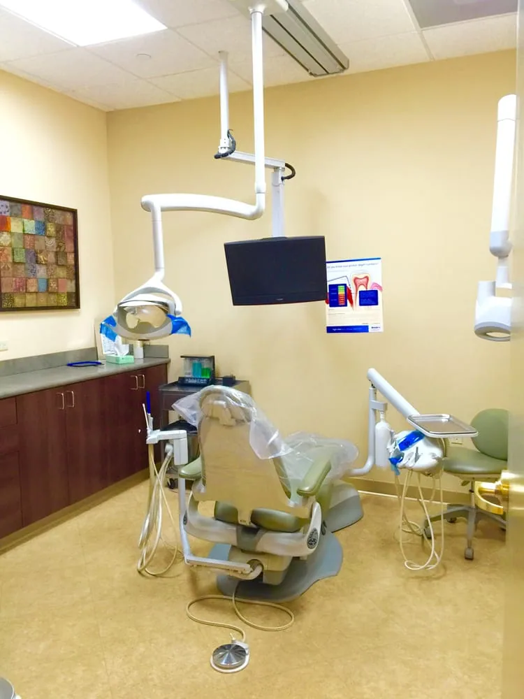 Treatment room with a dental chair, an overhead light and a wall-mounted monitor